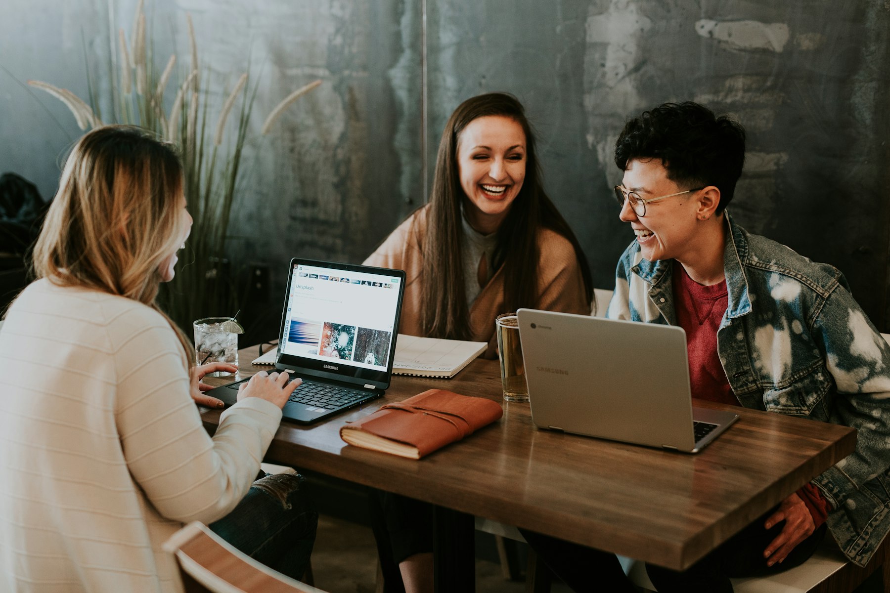 Drei junge Menschen arbeiten gemeinsam an Laptops und lachen